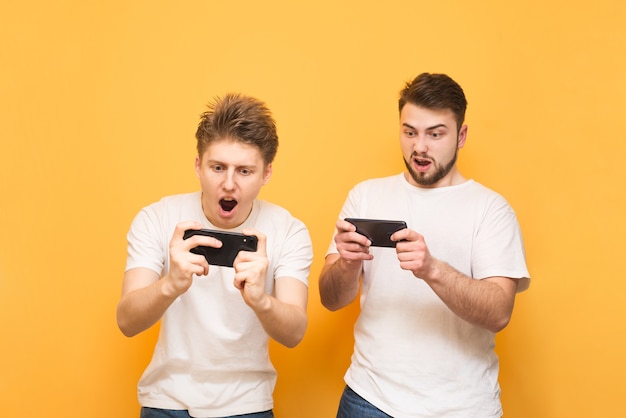 Dois meninos emocionados estão no amarelo e jogam jogos para celular em smartphones