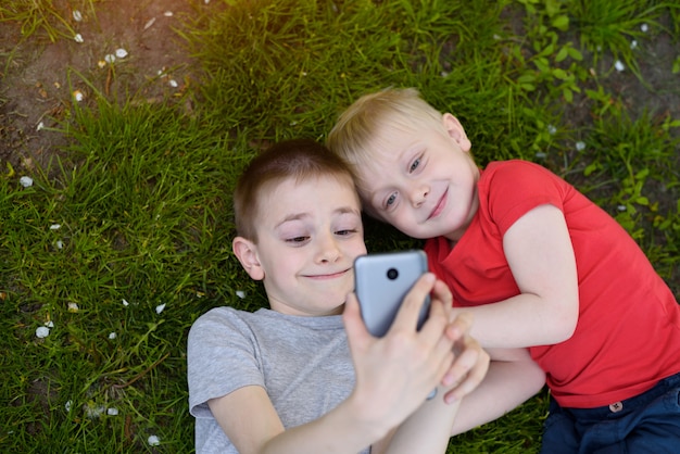 Dois meninos fazendo uma selfie com um smartphone deitado na grama.
