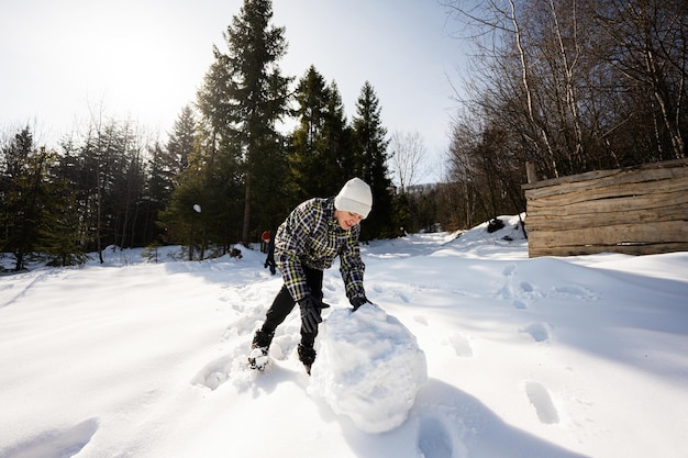 Dois meninos felizes juntos esculpem o globo de neve para o jogo dos irmãos de boneco de neve ao ar livre no inverno com neve nas montanhas