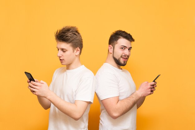 Dois meninos ficam de costas um para o outro no amarelo, segurando smartphones nas mãos, um olha para a tela