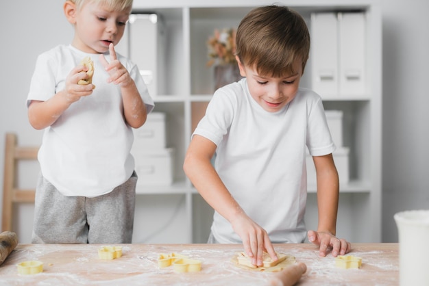 Dois meninos - irmãos preparam com entusiasmo biscoitos caseiros usando formas culinárias e cortam estatuetas da massa.
