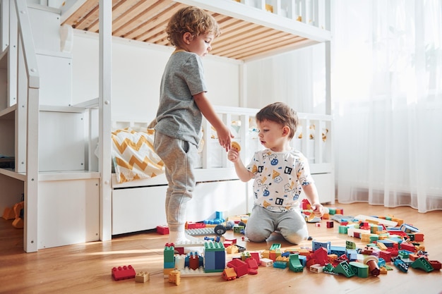 Dois meninos se divertem dentro de casa no quarto com conjunto de construção de plástico