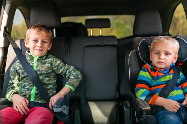 Dois meninos sentados em um assento de carro e um assento elevatório afivelados no carro.