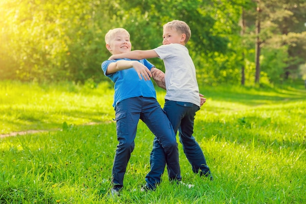 Dois meninos sorridentes loiros estão brigando no parque em um dia ensolarado