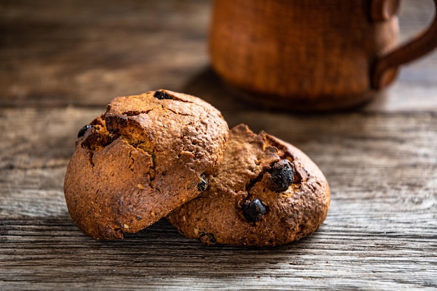 Dois muffins em uma mesa de madeira com um pote de gotas de chocolate