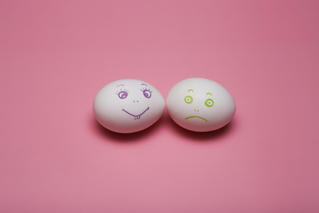 Dois ovos brancos expressão facial triste e alegre desenhada emoticon. Otimista e pessimista. Em um fundo rosa para a Páscoa. Foto de alta qualidade