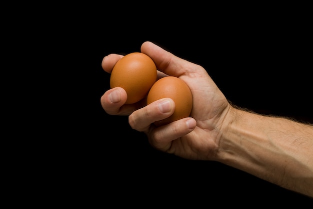Dois ovos em uma mão do homem, marrom, ovos, fundo preto