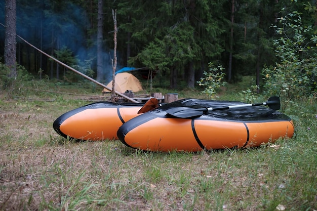 Dois packrafts estão para secar no acampamento na floresta contra o pano de fundo de uma tenda e fumaça de uma fogueira