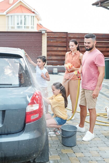 Dois pais olhando para os filhos ajudando-os a lavar o carro ao ar livre