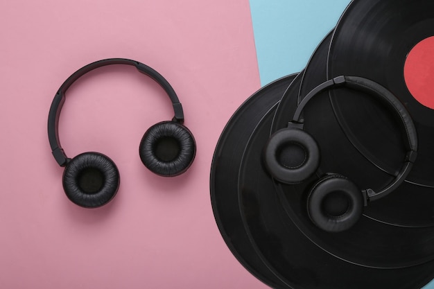 Dois pares de fones de ouvido estéreo pretos e discos de vinil em um fundo rosa azul