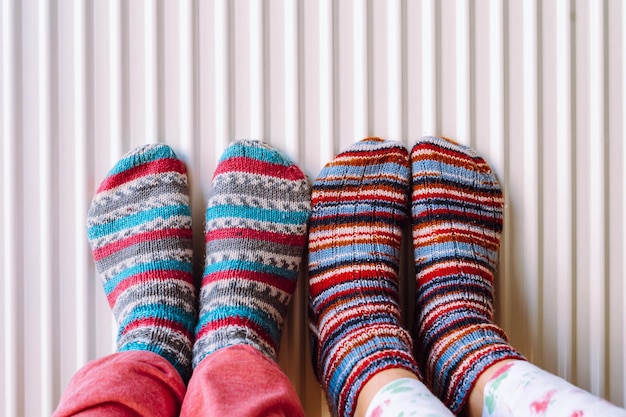 Dois pares de pernas em meias de malha feitas de fios de lã multicoloridos no radiador de aquecimento