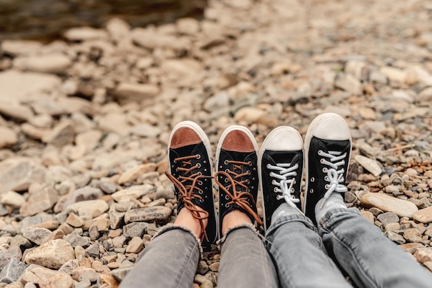 Dois pares de pernas em sapatos desportivos pretos apoiados em pedras ao ar livre