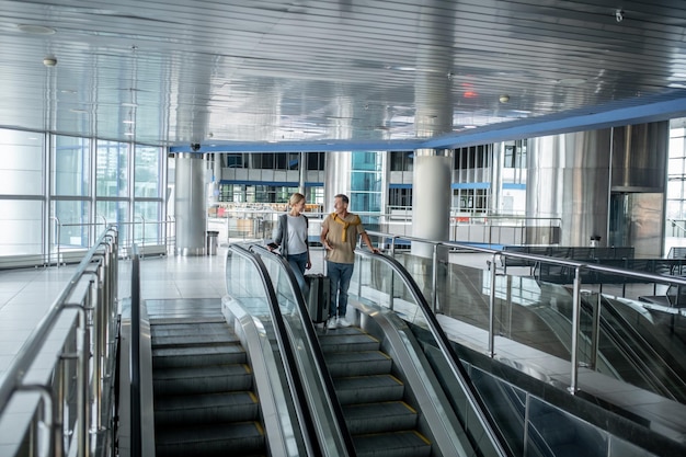 Foto dois passageiros do aeroporto conversando na escada rolante