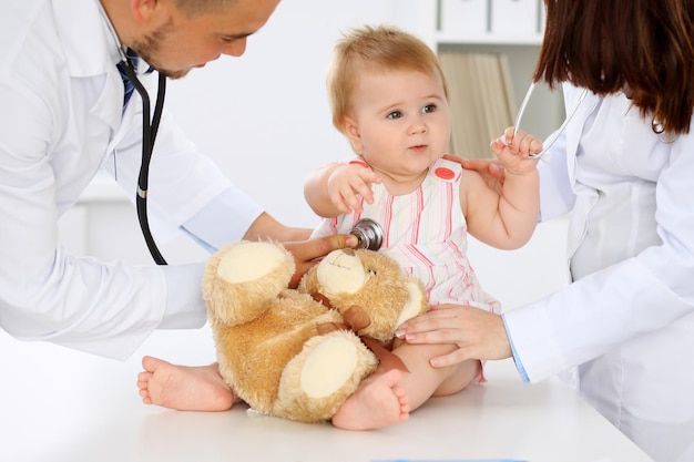 Dois pediatras estão cuidando do bebê no hospital A menina está sendo examinada pelo médico com estetoscópio Seguro de saúde e conceito de ajuda