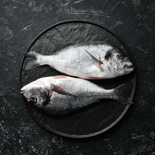 Dois peixes dourados com especiarias em uma placa de pedra preta Em um fundo escuro Vista superior