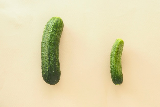 Dois pepinos verdes sobre um fundo bege. conceito de diferentes tamanhos de pênis masculino.