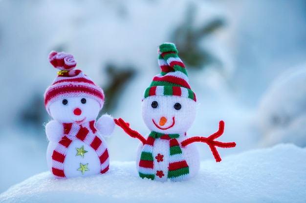 Dois pequenos brinquedos engraçados bebê boneco de neve em chapéus de malha e lenços na neve profunda ao ar livre em azul e branco brilhante cópia espaço fundo. cartão de feliz ano novo e feliz natal.