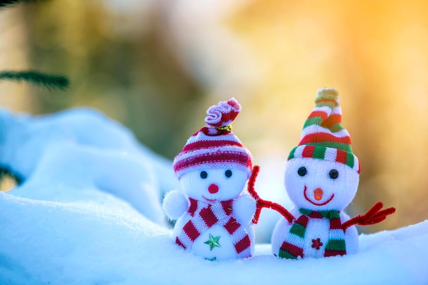 Dois pequenos brinquedos engraçados boneco de neve em chapéus de malha e cachecóis na neve profunda ao ar livre no fundo do espaço de cópia azul e branco brilhante Feliz Ano Novo e Feliz Natal cartão