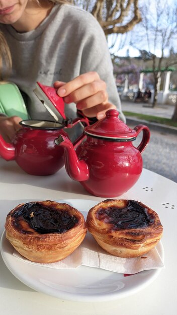 Dois pequenos bules com chá e dois bolos nacionais portugueses sobre uma mesa num café e uma rapariga no
