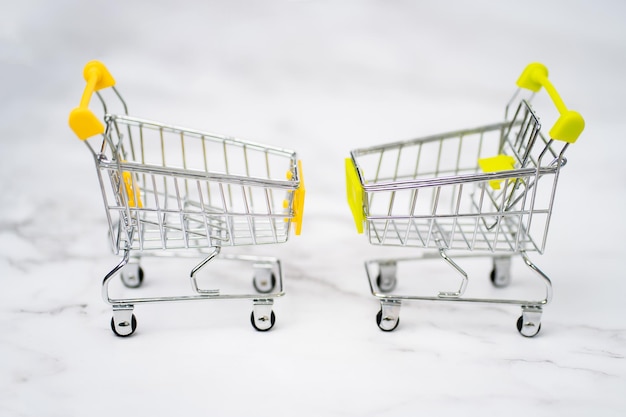 Dois pequenos carrinho de compras de brinquedo em miniatura de aço inoxidável vazio na mesa de mármore. Carrinhos de compras de supermercado em fundo branco. Shopping, shopping, conceito de negócio.