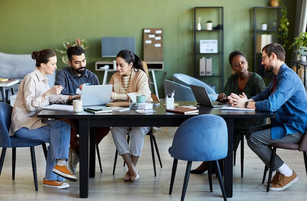 Dois pequenos grupos de designers criativos modernos discutindo pontos de trabalho enquanto estão sentados à mesa em fr