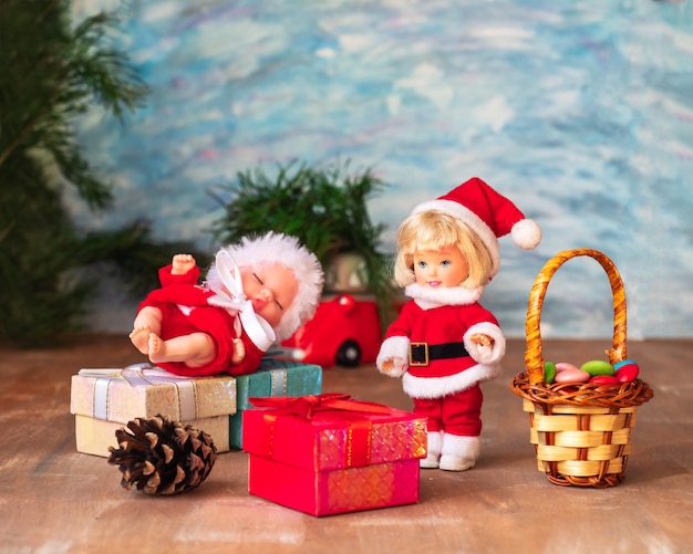 Dois pequenos papai noel ao lado de caixas com presentes de uma árvore de Natal em um fundo de madeira