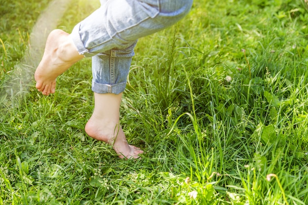 Dois pés femininos bonitos andando na grama na manhã ensolarada de verão. Pés claros da menina da etapa descalça no gramado macio da mola no jardim ou no parque. Liberdade saudável relaxar conceito.