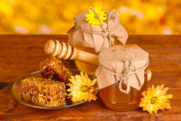 Dois potes de favos de mel e chuvisco de madeira na mesa em fundo amarelo
