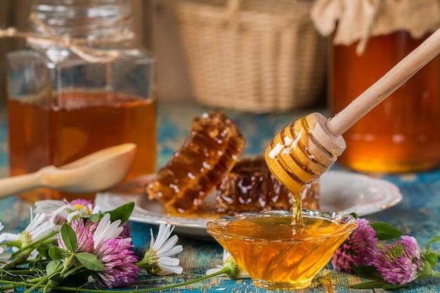 Dois potes de mel com favo de mel em uma mesa de madeira com flores