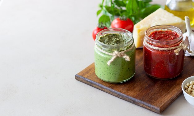 Dois potes de vidro com pesto vermelho e pesto de manjericão. Cozinha nacional. Alimentação saudável. Comida vegetariana.