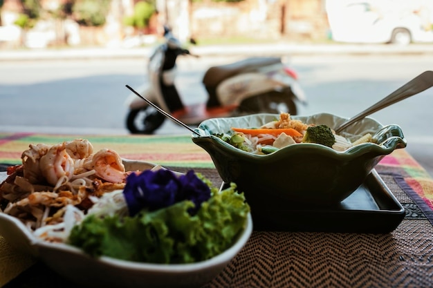 Dois pratos de comida tailandesa picante na varanda da rua Na motocicleta de fundo