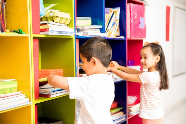 Dois pré-escolares pegando seus livros em um armário de sala de aula e se preparando para a aula