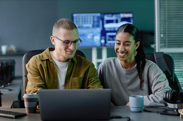 Dois programadores sorridente cooperando usando laptop na mesa durante reunião de trabalho no escritório