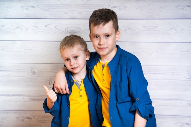 Dois rapazes atraentes em camisas azuis e camisetas amarelas, posando juntos. Retrato de dois irmãos, abraçando e olhando