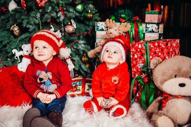 Dois rapazes sentam-se entre os presentes antes de uma árvore de Natal