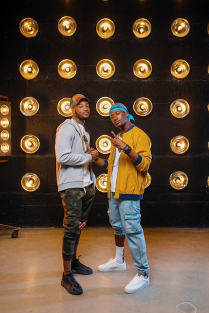 Dois rappers negros em bonés, artistas posam no palco