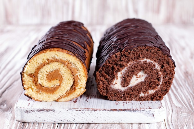 Foto dois rolos de biscoito. pão de ló de chocolate e creme branco na tábua de madeira