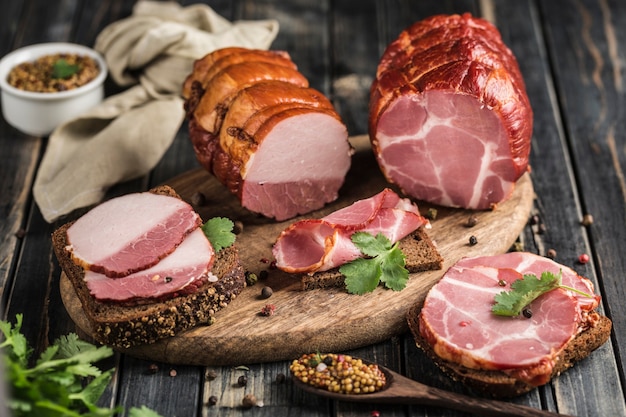 Foto dois rolos de carne de porco e carne fatiada com fatias de pão em uma placa de madeira em um fundo escuro. carne de porco defumada. vista lateral. orientação horizontal com um espaço de cópia para o texto.