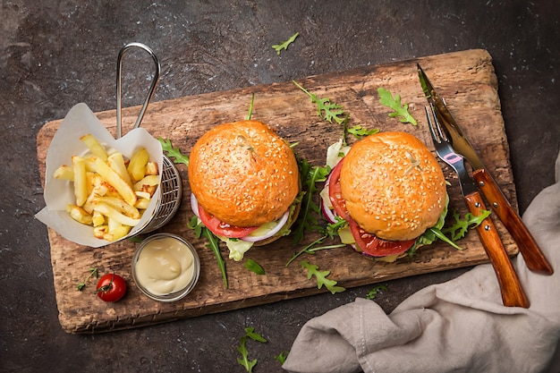 Dois saborosos hambúrgueres clássicos de carne grelhada com batatas fritas em uma mesa rústica preta com espaço de cópia