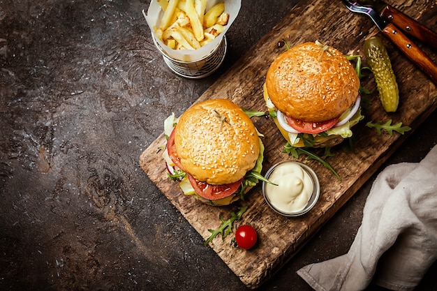 Dois saborosos hambúrgueres clássicos de carne grelhada com batatas fritas em uma mesa rústica preta com espaço de cópia