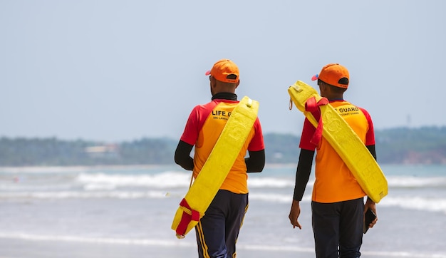 Foto dois salva-vidas de plantão na praia tropical, ambos carregando tubos de resgate nos ombros e caminhando em weligama, sri lanka