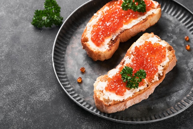 Dois sanduíches com caviar vermelho Caviar vermelho salmão na tigela e servidor de sanduíches na chapa de ferro velha no fundo da mesa preta velha Vista superior Espaço para cópia