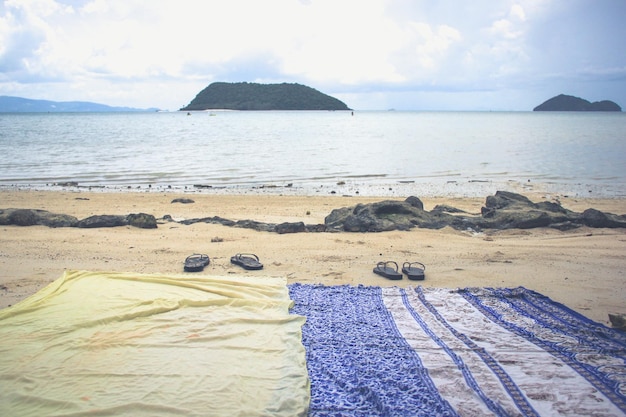 Dois sarongues de praia e chinelos na areia pela costa no mar calmo e vazio ao pôr do sol na ilha da Tailândia