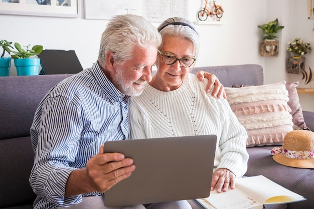 Dois seniores ficam em casa olhando juntos para o laptop. Um casal de idosos, conceito de prevenção e positividade