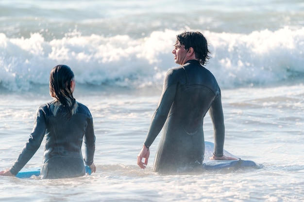 dois surfistas latinos andando no oceano para surfar as ondas, vista traseira