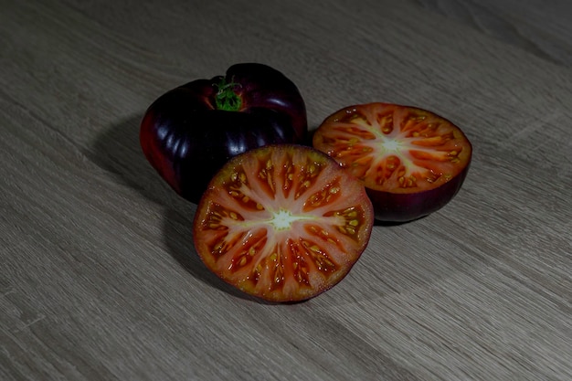 Foto dois tomates azuis numa mesa de madeira, um inteiro, recém colhido, e o outro cortado ao meio.