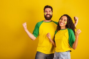 Foto dois torcedores do futebol brasileiro vestidos com as cores da nação mulher negra homem caucasiano torcendo e vibrando