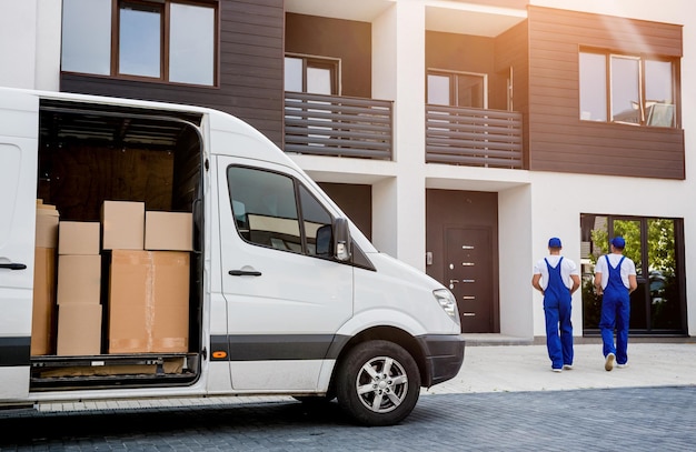 Dois trabalhadores da empresa de mudanças descarregando caixas do microônibus para a nova casa