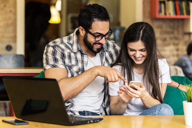 Dois trabalhadores de escritório homem barbudo de óculos e menina morena se divertindo assistindo fotos tiradas no smartphone