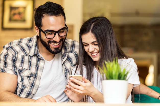 Dois trabalhadores de escritório homem barbudo de óculos e menina morena se divertindo assistindo fotos tiradas no smartphone